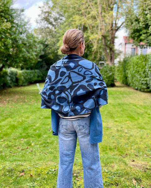 A person wearing a striped shirt with a navy blue and black scarf featuring a wild dog print wrapped around body