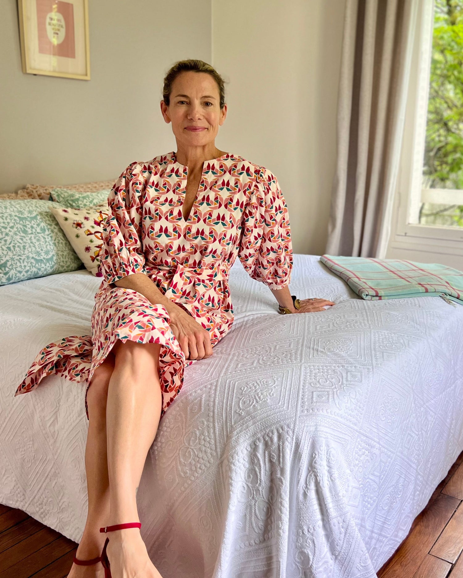 Woman sitting on a bed wearing a multi-colored block-printed puff sleeve dress 