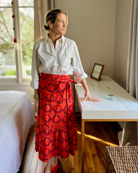 A person wearing a red and purple geometric patterned skirt with a wrap-around style and a white button-down