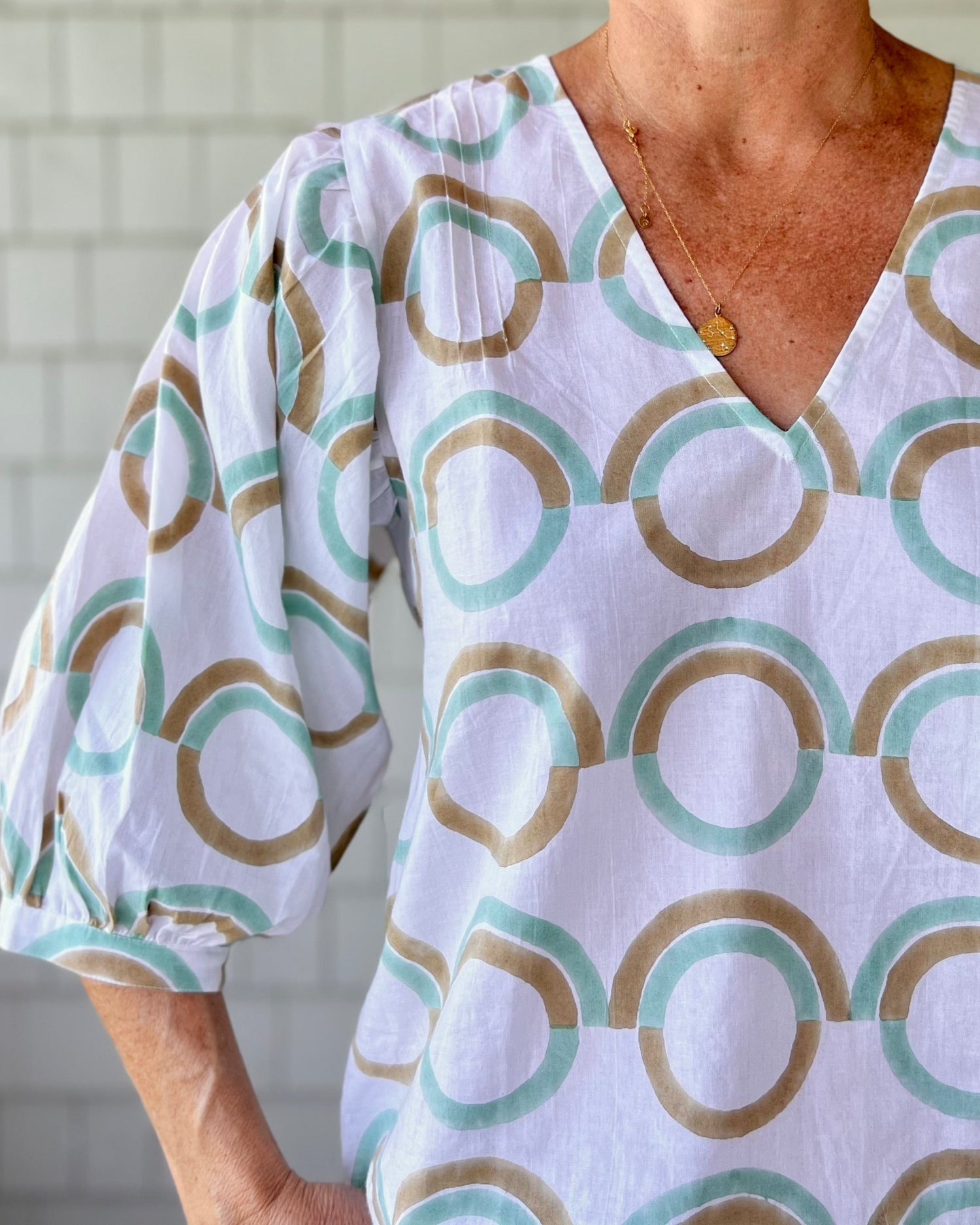 A woman standing outdoors wearing a mint green blouse with puff sleeves, featuring a geometric pattern.