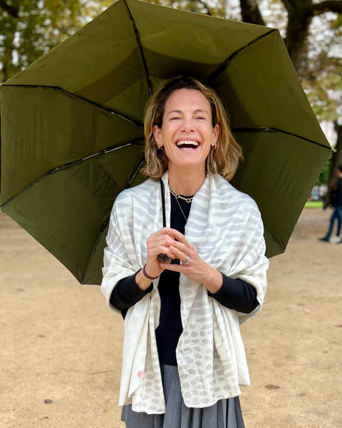 Smiling woman with green umbrella in Paris park wearing a white and light gray owl print wrap over black sweater