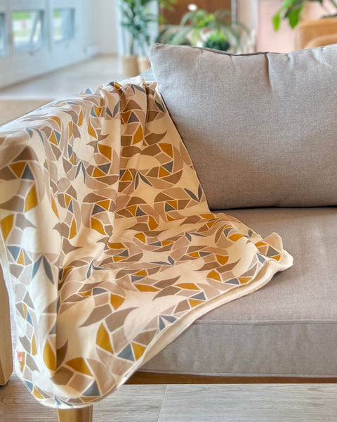 A chair with a cream-colored cozy wrap/scarf with a geometric pattern featuring mustard yellow, taupe, and gray blue