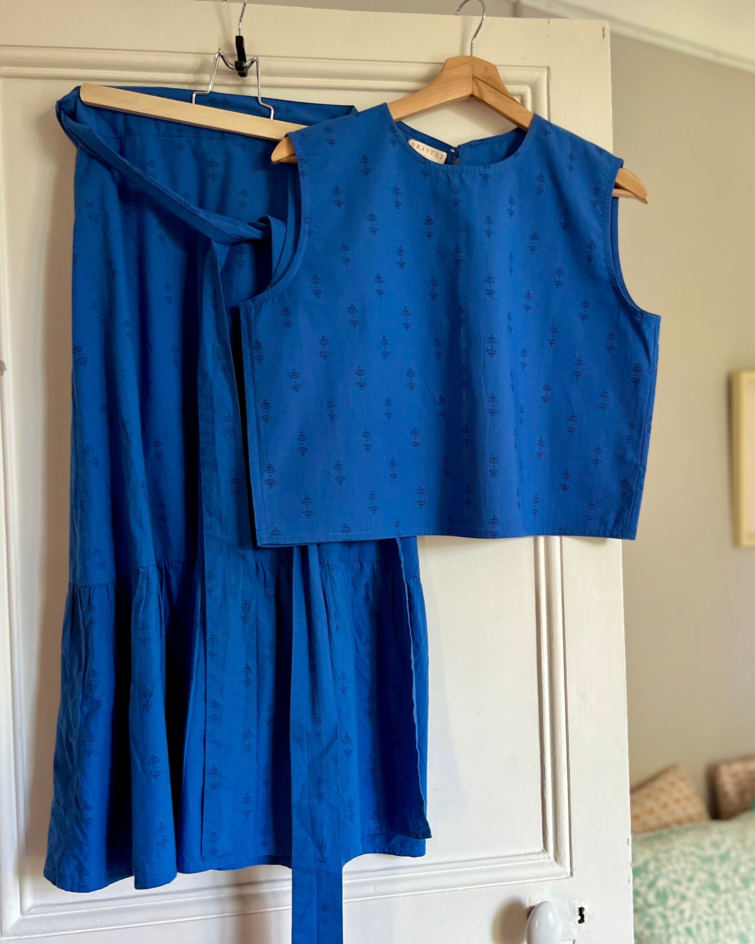 Blue outfit with top and skirt on a hanger against a white door.