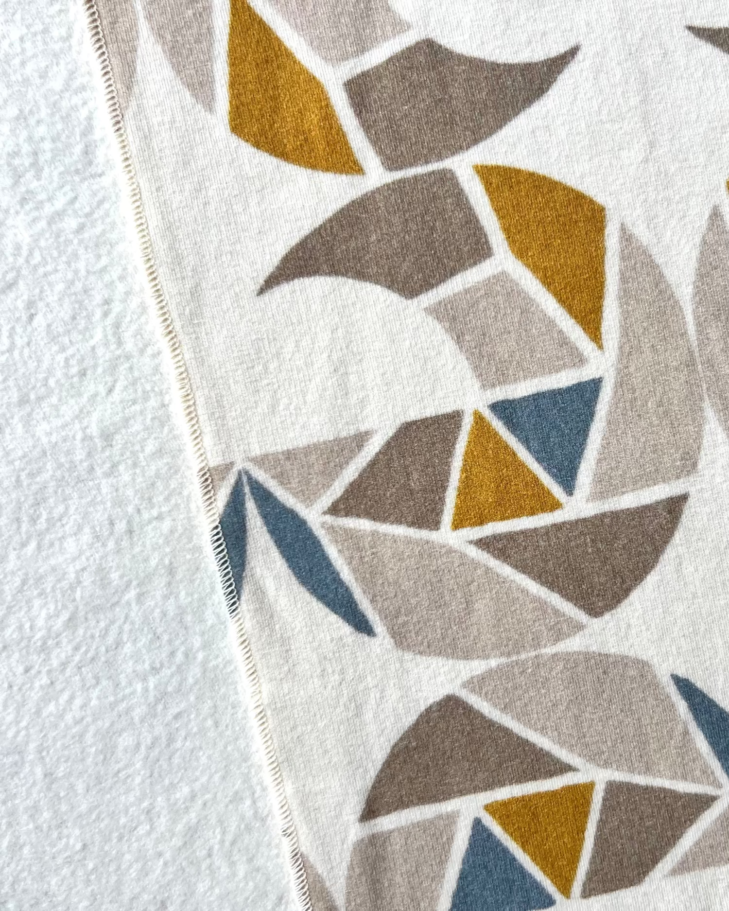 Close-up of a cream-colored cozy wrap/scarf with a geometric pattern featuring mustard yellow, taupe, and gray blue