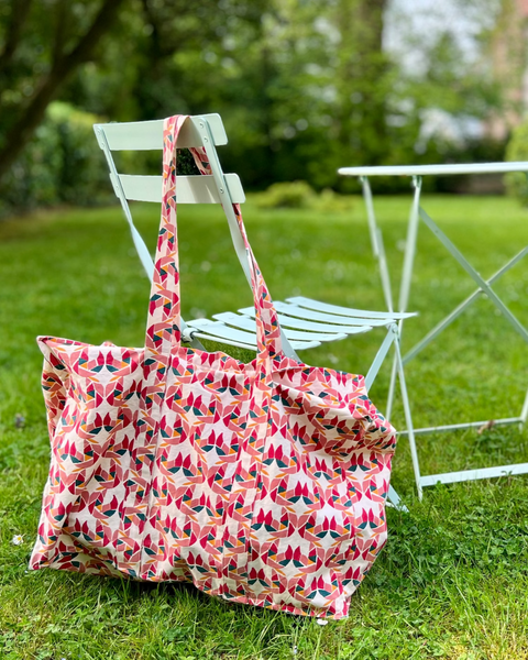 A tote bag with a colorful block-printed pattern featuring mollusks, hanging on a garden chair.
