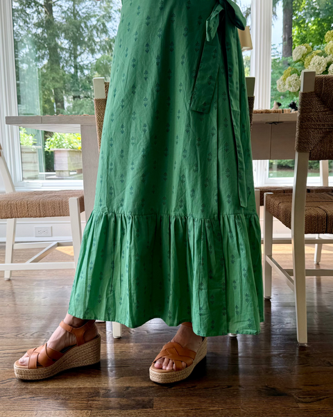 Person wearing a green hand block-printed maxi skirt with ruffled hem in a room with wooden flooring and chairs.