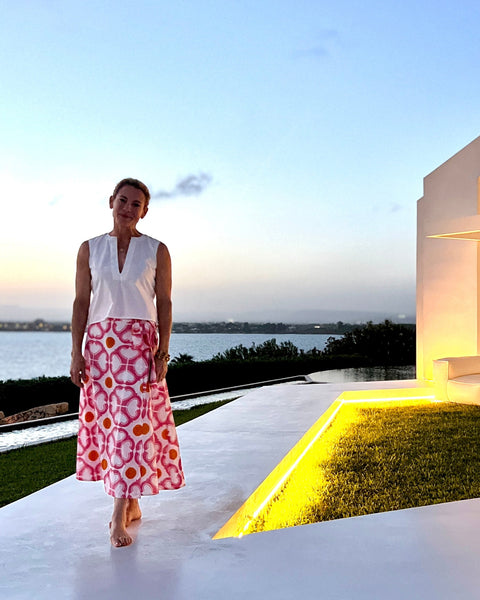 A woman wearing a watermelon pink and orange condor wrap skirt with a tea length cut and a white top at sunset