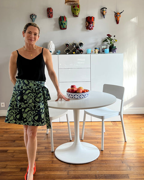 A person wearing a green wrap skirt with an animal print in navy blue, paired with a black top, standing in a room with natural lighting.