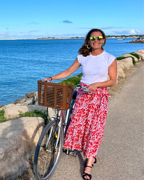 Woman wearing beautiful red and purple block-printed wrap skirt standing next to a bicycle on a beautiful day by the water