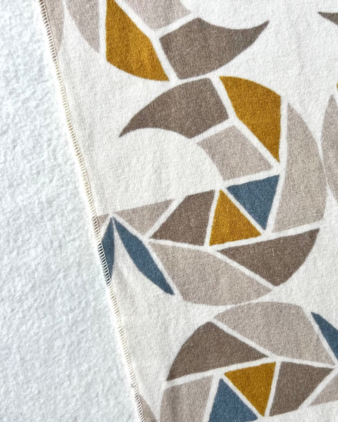 Close-up of a cream-colored cozy wrap/scarf with a geometric pattern featuring mustard yellow, taupe, and gray blue