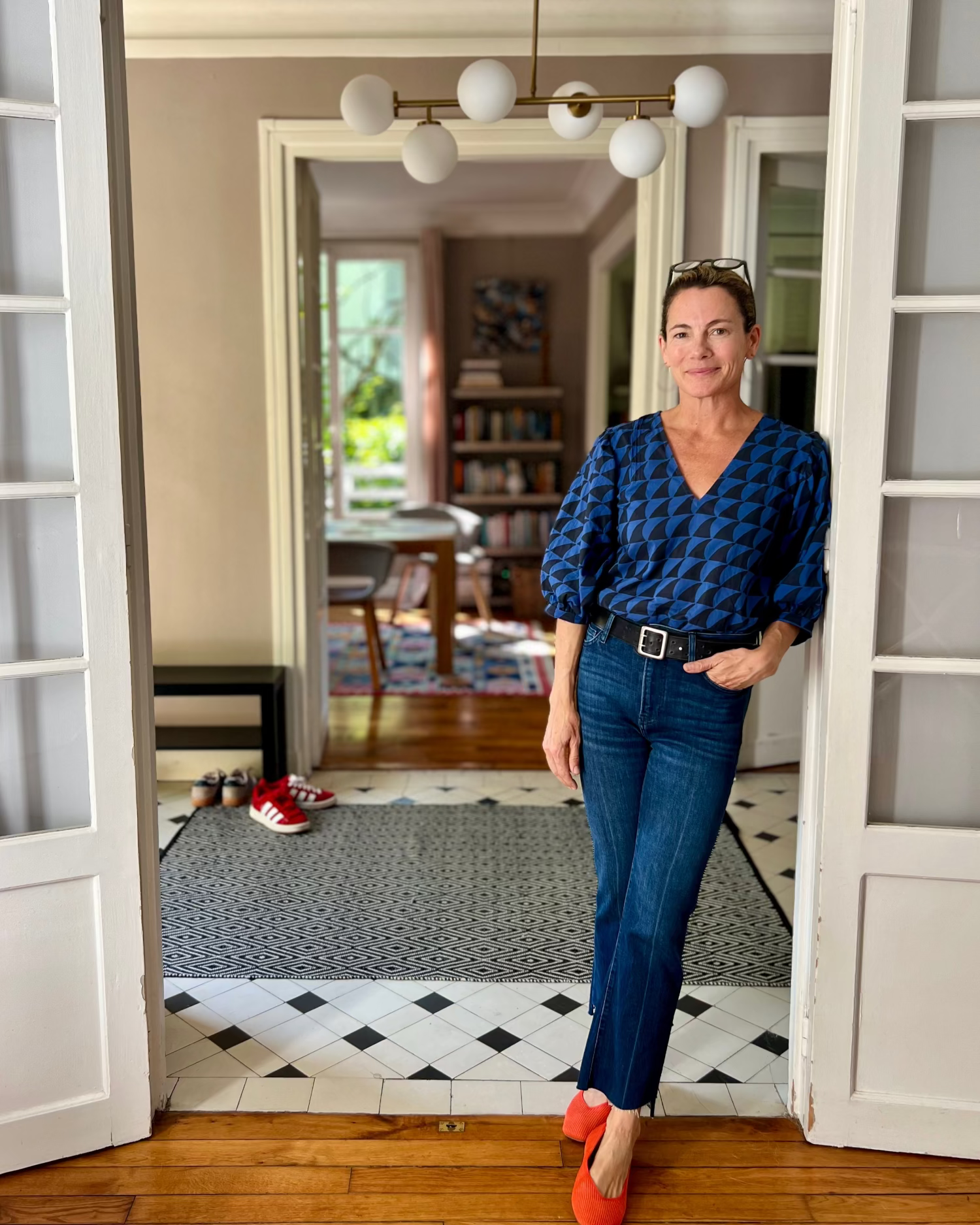 Woman standing in a home interior wearing a blue and black shark patterned blouse and jeans.