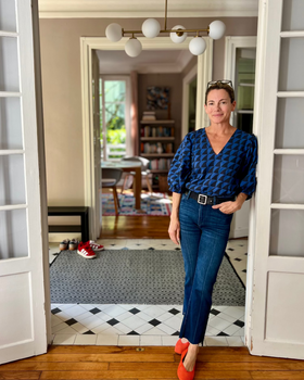 Woman standing in a home interior wearing a blue and black shark patterned blouse and jeans.