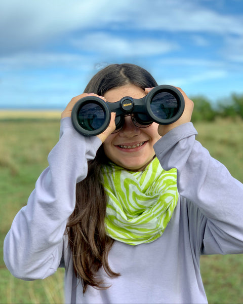 A person smiling with binoculars and wearing a chartreuse and ice blue faux bois infinity scarf