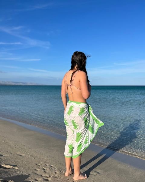 A person wearing a hand block-printed grass green and white sarong / grand scarf standing with their back towards the camera on the beach