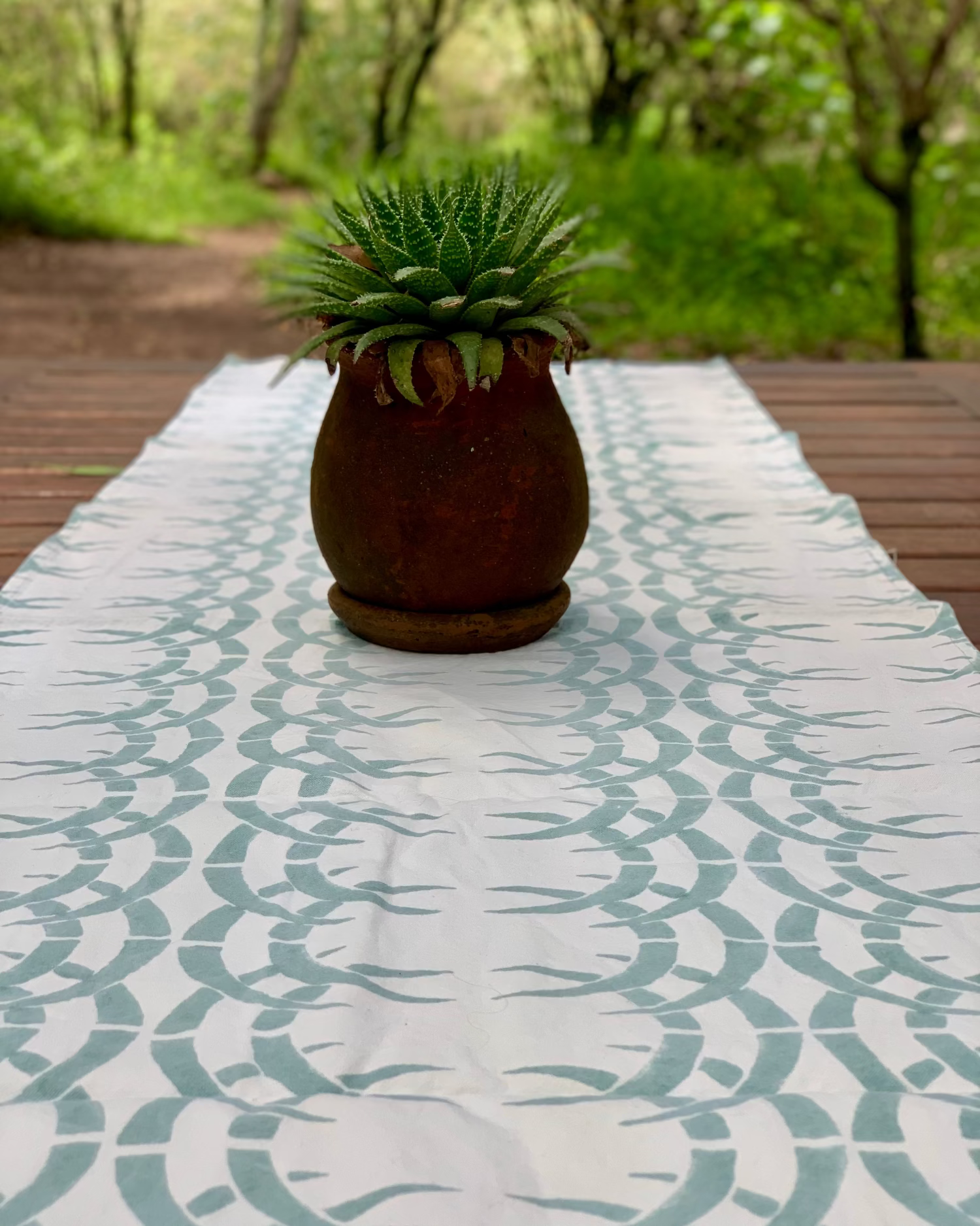 Potted plant on table with sage blue and ice blue rhino print table runner and forest in the background