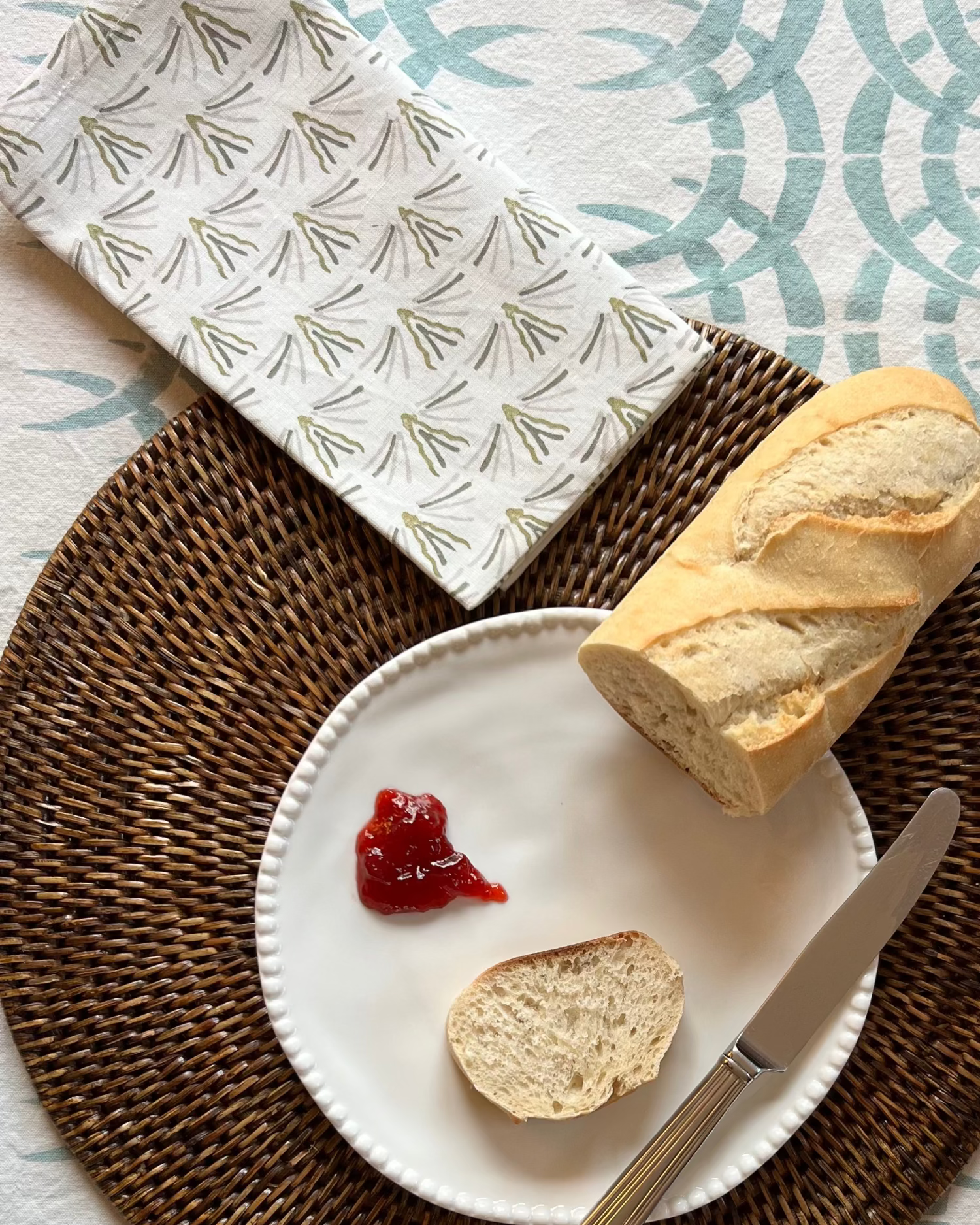 Baguette and jam, placed on a woven placemat with a organic cotton napkin and tablecloth.