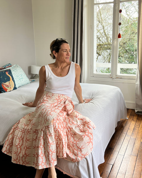 A person sitting on a bed wearing a peach-colored wrap skirt with a rhino and horn pattern, paired with a white top.