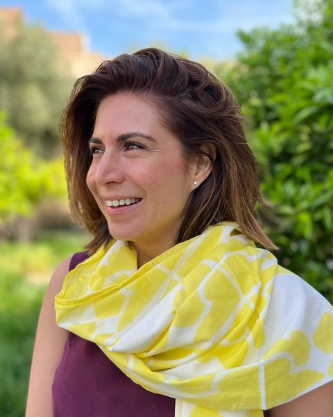 Woman wearing lemon yellow and white hand block-printed sarong / grand scarf outdoors with greenery in the background