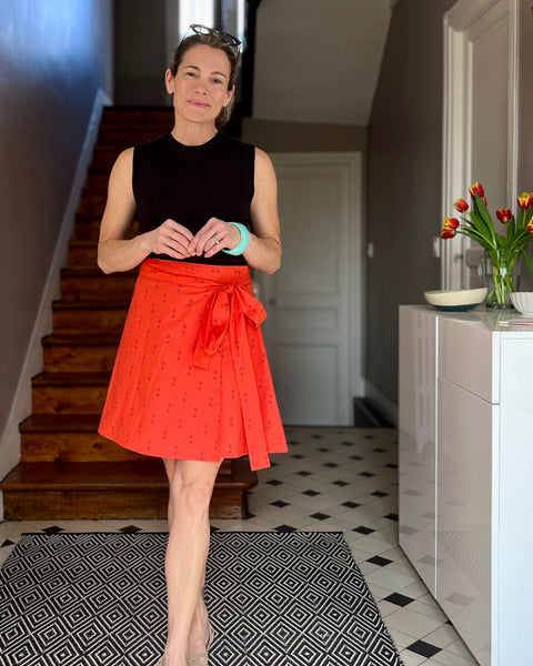A person wearing a red wrap skirt with a purple block-printed pattern, paired with a black top, standing in a home entrance.