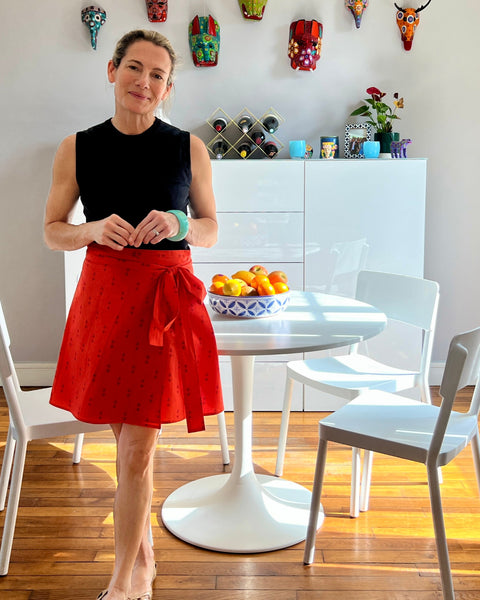A person wearing a red wrap skirt with a purple block-printed pattern, paired with a black top, standing in a dining room