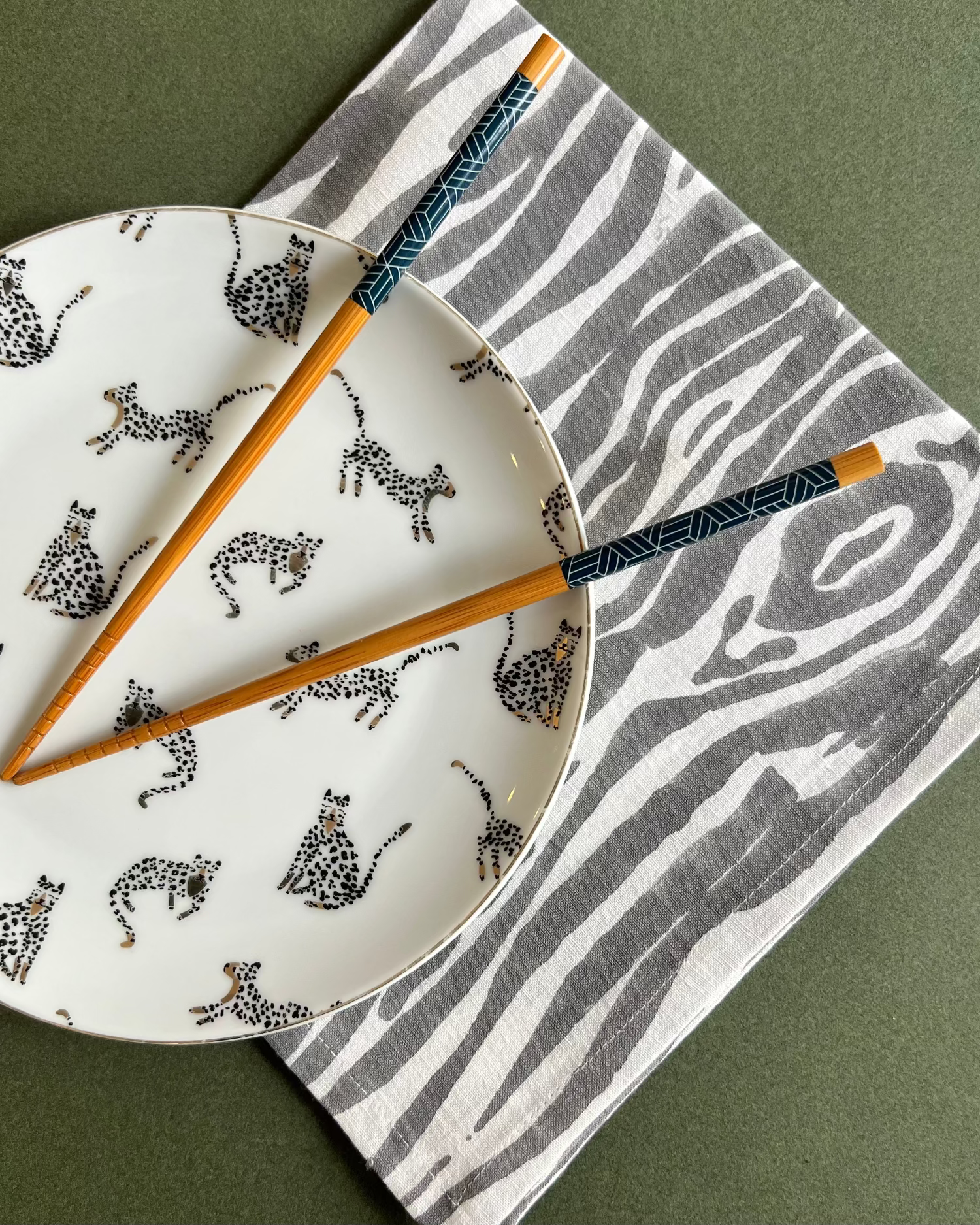 White plate with black animal pattern, wooden chopsticks, and gray and white faux bois napkin on a green surface