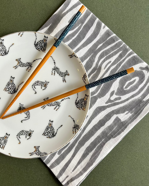 White plate with black animal pattern, wooden chopsticks, and gray and white faux bois napkin on a green surface