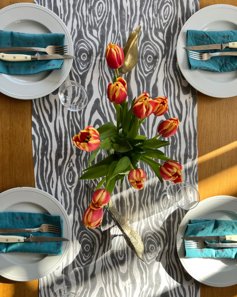 Dining table setting with tulips, plates, and cutlery on a gray and white faux bois hand block-printed organic cotton linen table runner with teal napkins