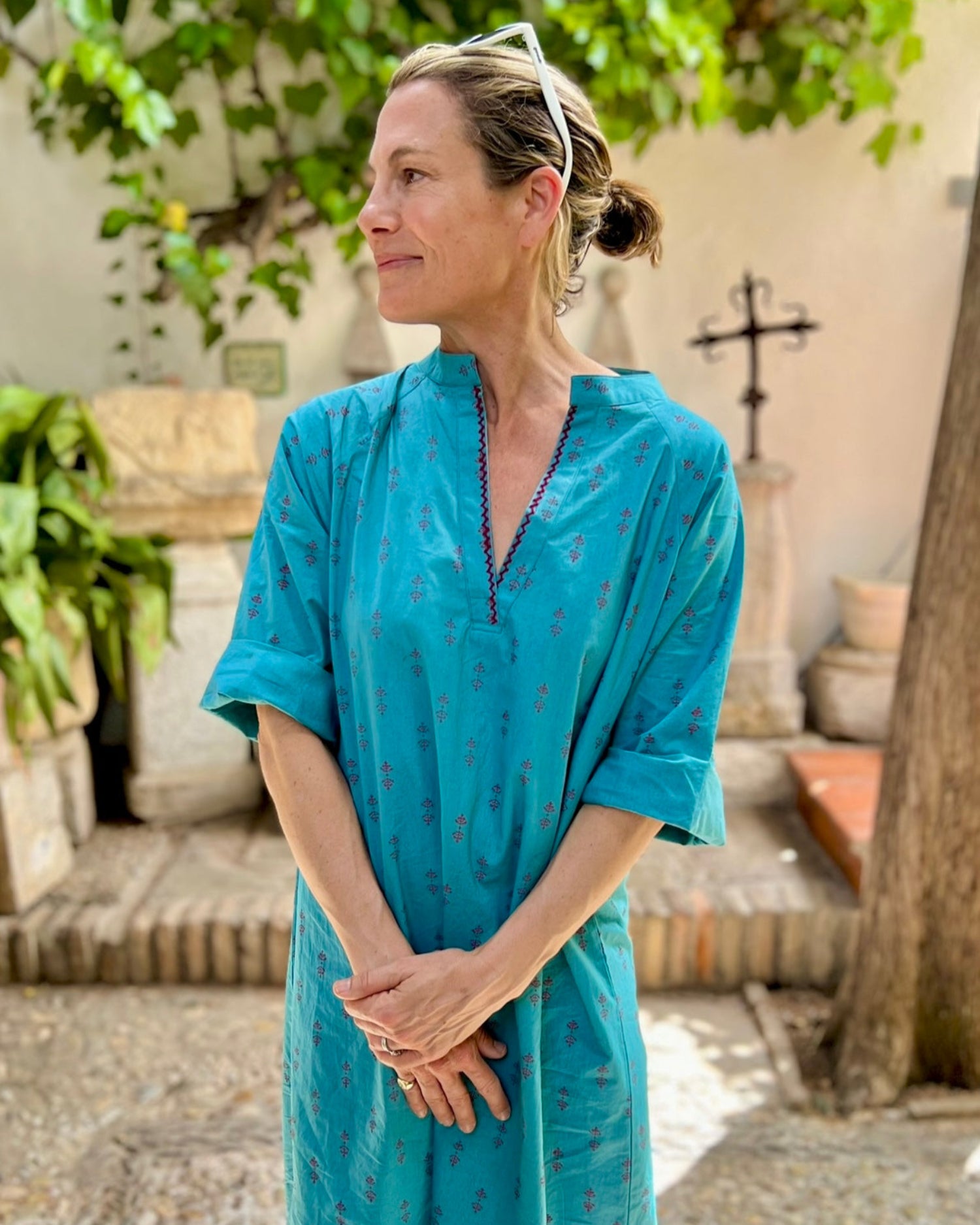 Woman wearing a teal block-printed dress standing outdoors with greenery in the background