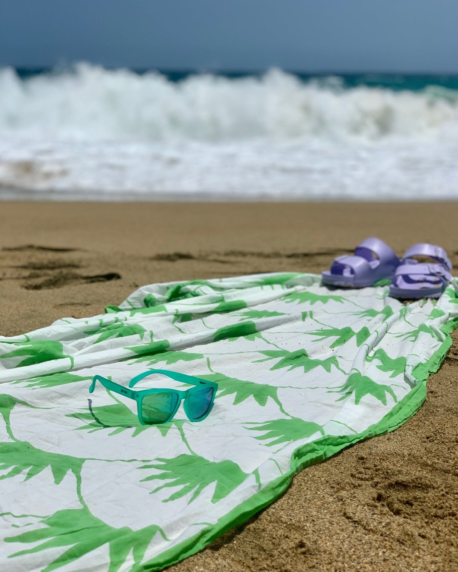 Hand block-printed grass green and white sarong on the beach with Goodr sunglasses and lavender Birkenstocks