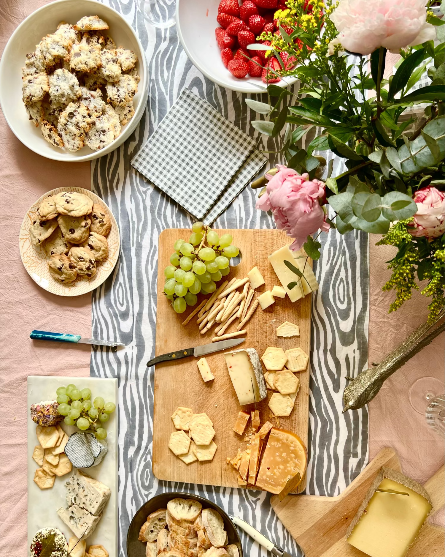 Table setting with cheeseboard, crackers, grapes, and flowers on a gray and white faux bois hand block-printed organic cotton linen table runner and blush pink tablecloth