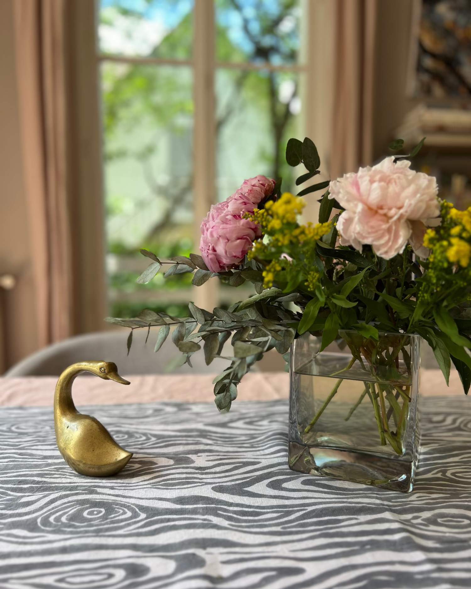 Decorative vase with flowers and a brass swan on a table with a gray and white faux bois hand block-printed organic cotton linen table runner 