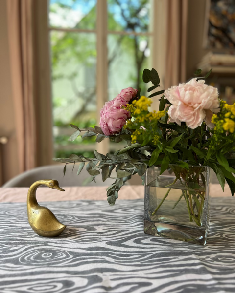 Decorative vase with flowers and a brass swan on a table with a gray and white faux bois hand block-printed organic cotton linen table runner 