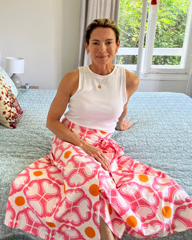 A person seated on a bed wearing a watermelon pink and orange condor wrap skirt with a tea length cut.