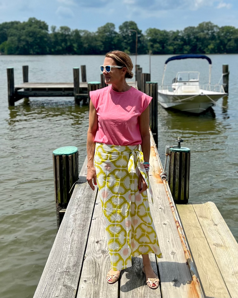 A person on a dock wearing a wrap skirt with a geometric pattern in yellow and pink on an off-white background and a pink shirt
