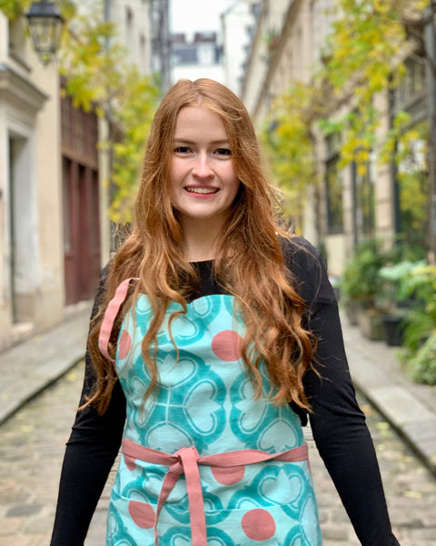 Woman wearing a turquoise and terracotta hand block-printed apron with adjustable ties and pockets in a beautiful walkway in Paris
