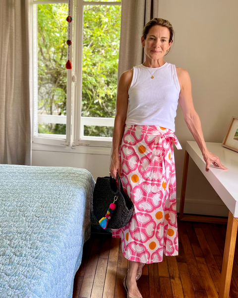 A woman wearing a watermelon pink and orange condor wrap skirt with a tea length cut and a white top