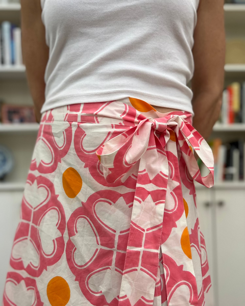 A woman wearing a watermelon pink and orange condor wrap skirt with a tea length cut and a white top