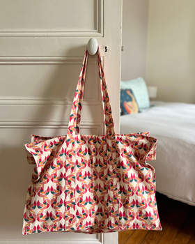 A tote bag with a colorful block-printed pattern featuring mollusks, displayed in a home environment.