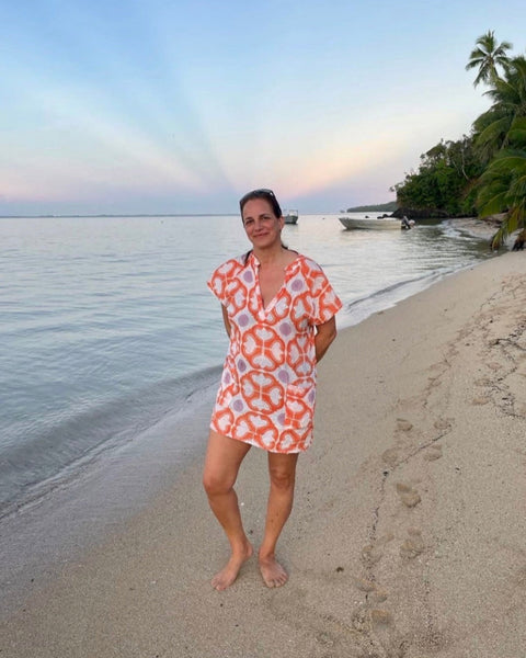 Woman on a beach wearing a coral, lavender, and white hand block-printed short kaftan dress 