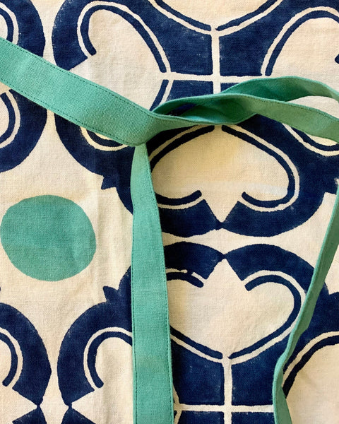 Close-up of a navy blue, green, and off-white block-printed apron with adjustable ties and pockets