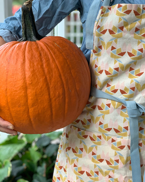 Woman wearing a hand block-printed apron with adjustable ties and pockets holding a pumpkin