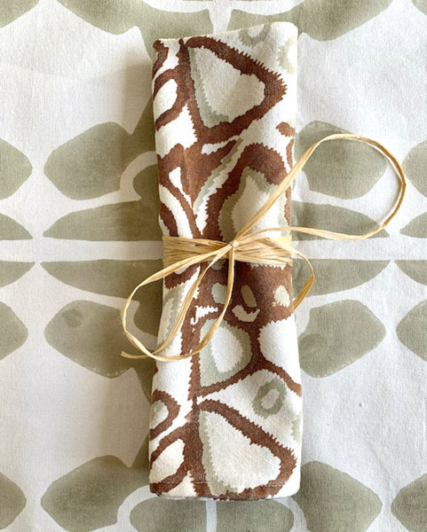 Rust, khaki, and white hand block-printed napkin rolled up on sand / khaki and white table runner
