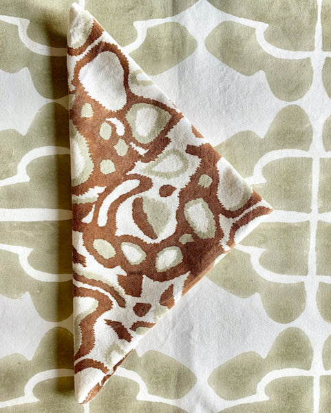 Rust, khaki, and white hand block-printed napkin folded on sand / khaki and white table runner