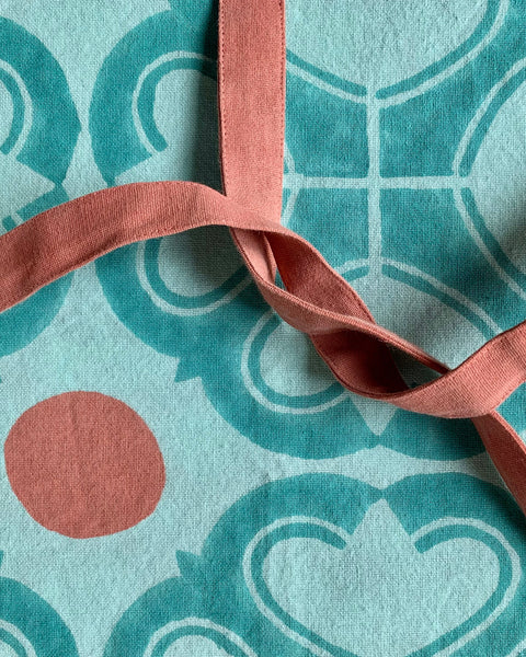 Close-up of a turquoise and terracotta hand block-printed apron with adjustable ties and pockets