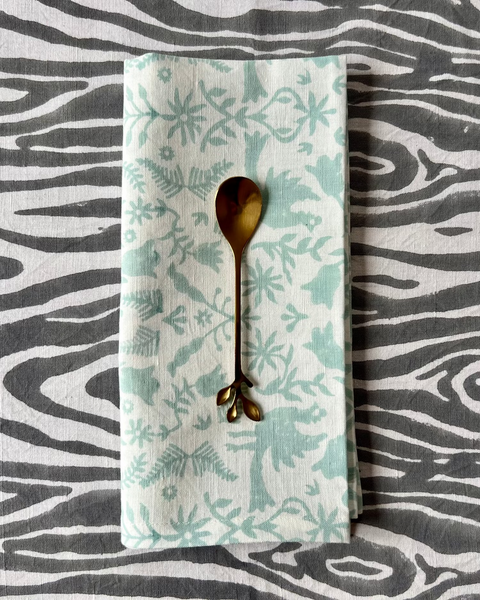 A folded organic cotton linen napkin with a mint blue pattern, displayed on a faux bois table runner.