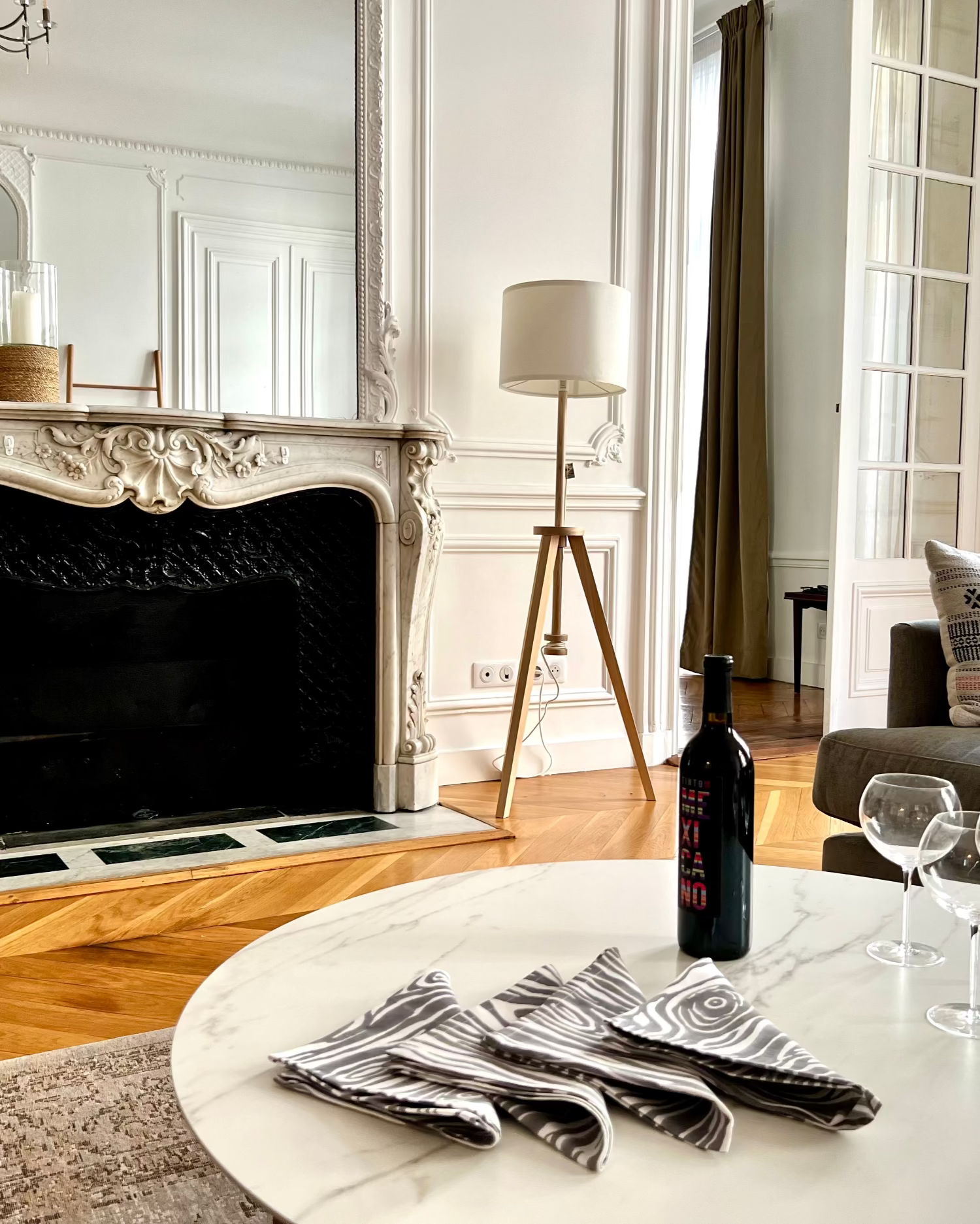 A set of gray and white faux bois print cotton linen napkins displayed on a table with cutlery, in a room with a fireplace and a mirror in the background.