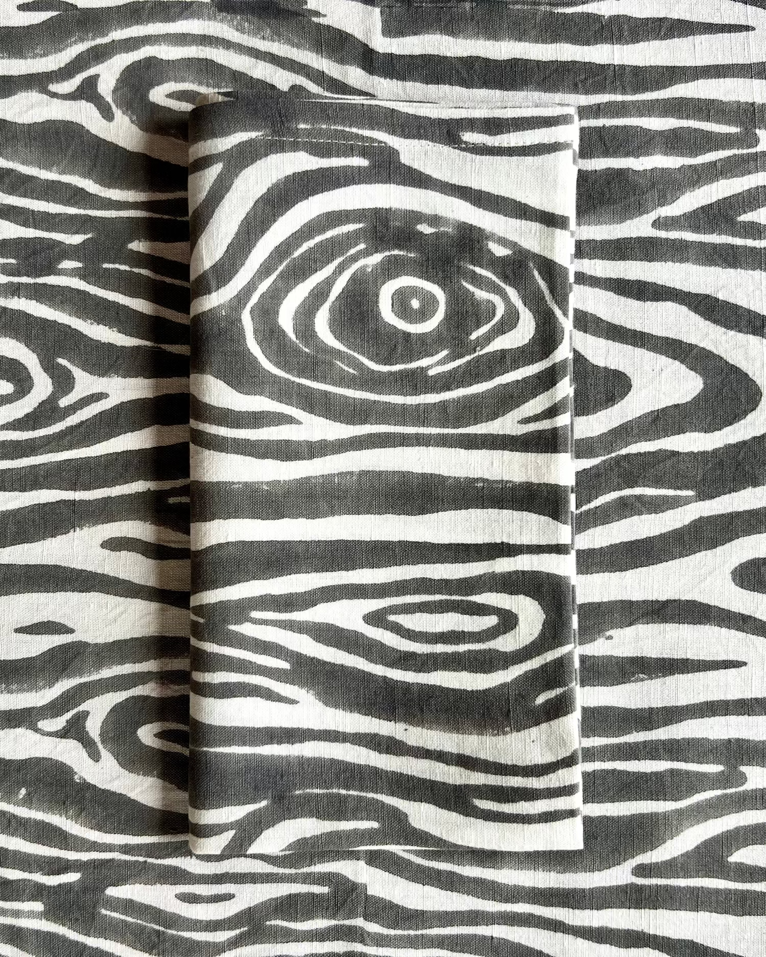 A gray and white faux bois print cotton linen napkin on a faux bois table runner
