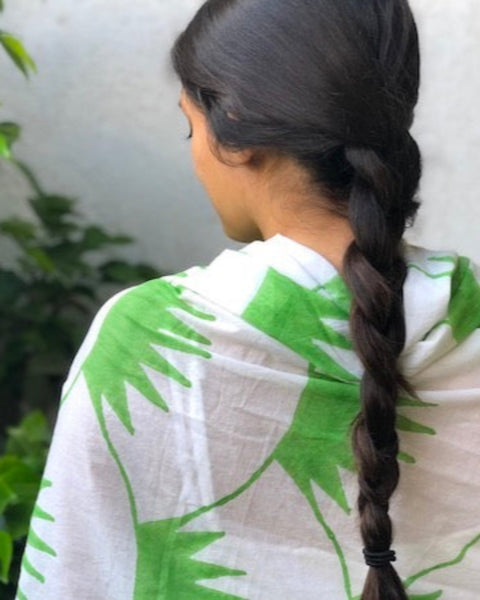 A person wearing a hand block-printed grass green and white sarong / grand scarf standing with their back towards the camera with green foliage in the background.
